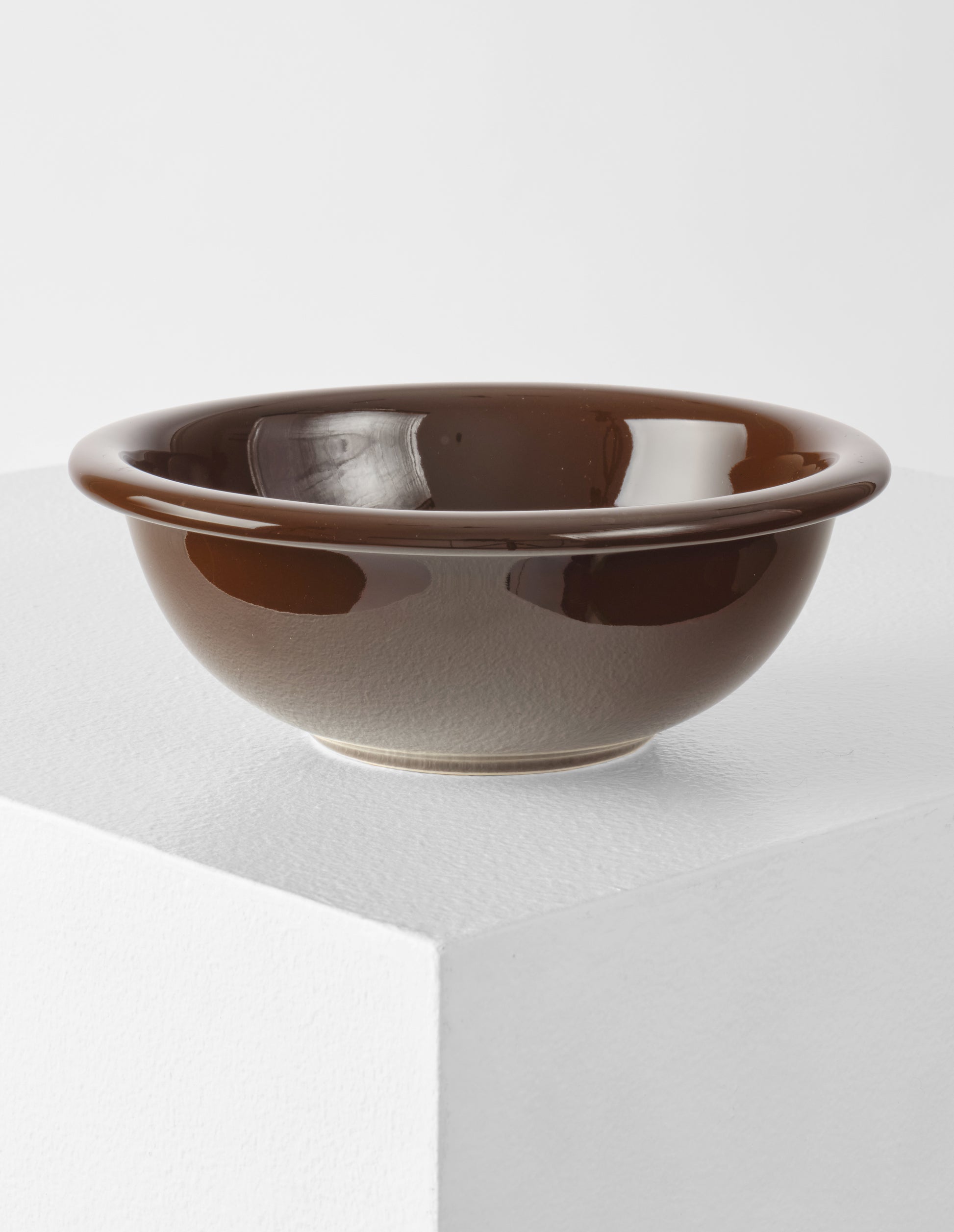 A single brown high gloss stoneware Bronto bowl on a white plinth.