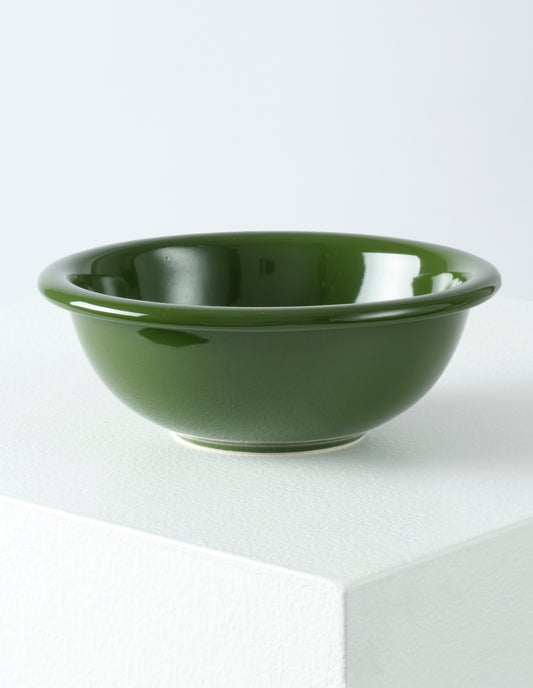 A single green high gloss stoneware Bronto bowl on a white plinth.