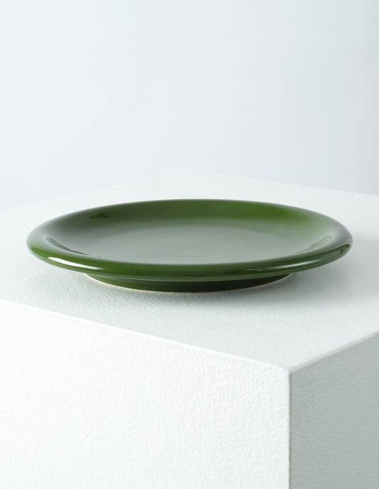 A single green high gloss stoneware Bronto plate on a white plinth.