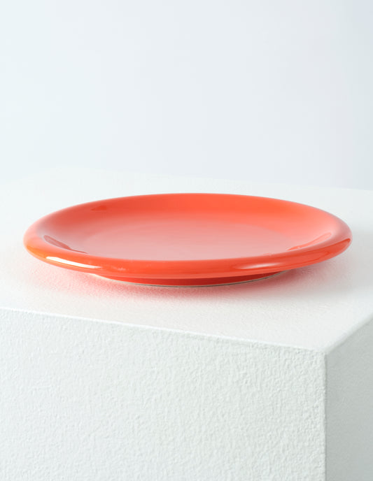 A single orange high gloss stoneware Bronto plate on a white plinth.