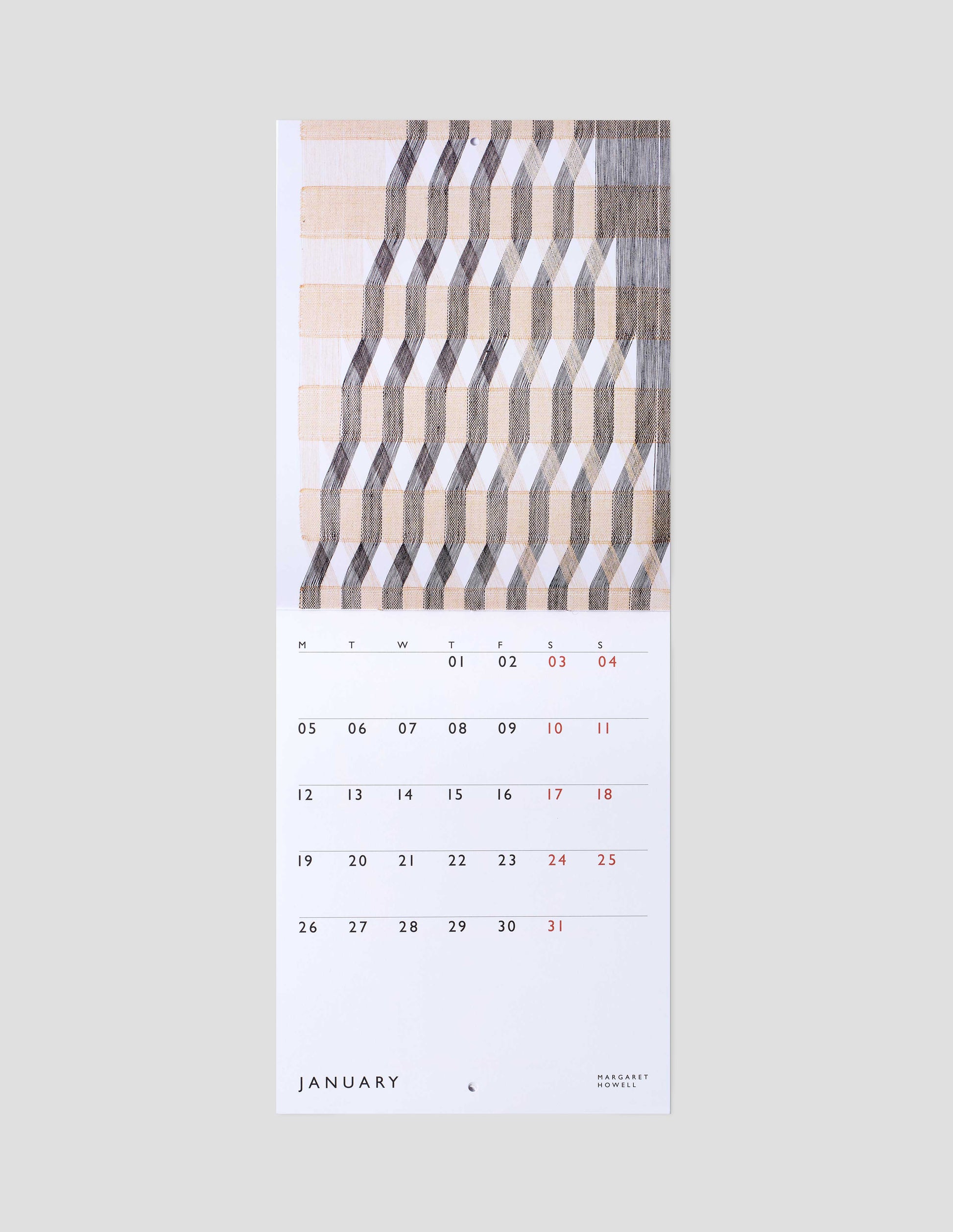 A flat lay view of calendar showing January double page spread, with a macrogauze wall hanging on one page and days of the month on a white background on the other.