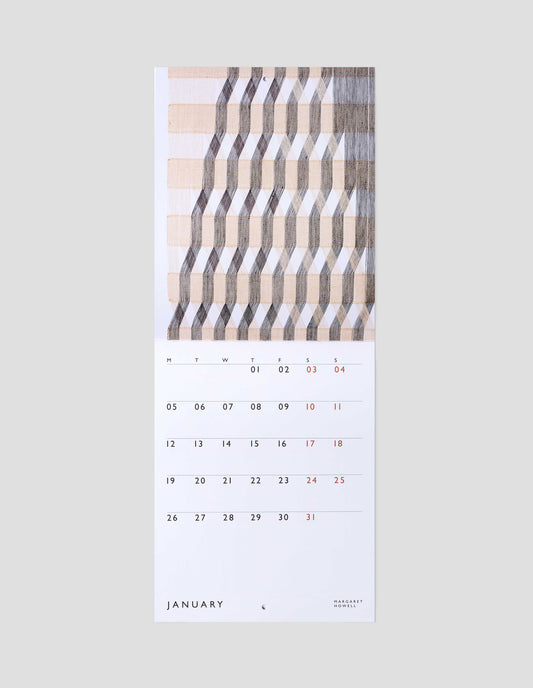 A flat lay view of calendar showing January double page spread, with a macrogauze wall hanging on one page and days of the month on a white background on the other.