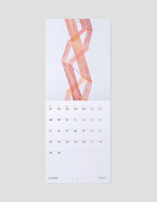 A flat lay view of calendar showing June double page spread, with a macrogauze wall hanging on one page and days of the month on a white background on the other.