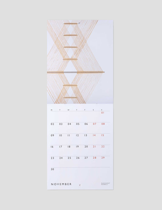 A flat lay view of calendar showing November double page spread, with a macrogauze wall hanging on one page and days of the month on a white background on the other.