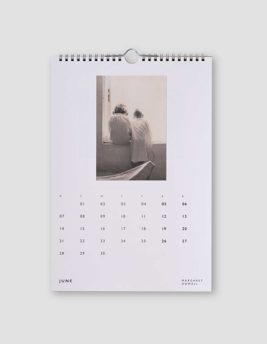 An image of a white page from the calendar featuring a black and white photograph of two children with their backs to the camera, and with days of the month under the image. Flat lay image on a light grey background.