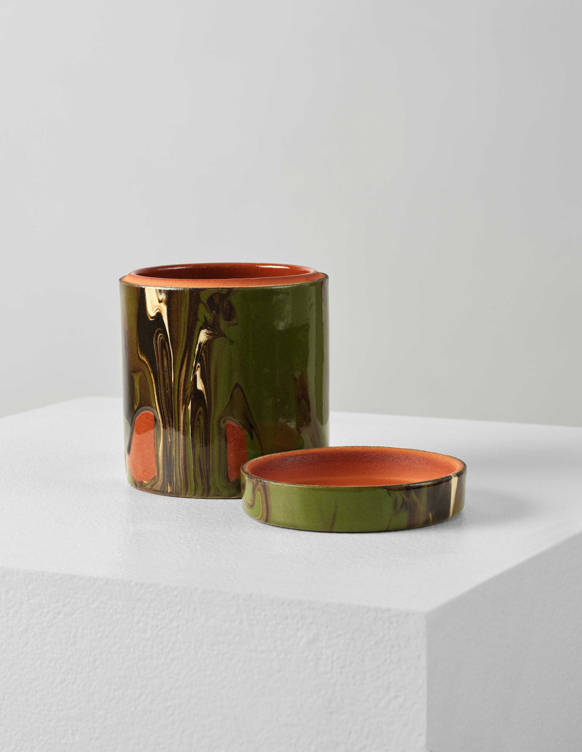 Front flat lay of a round ceramic green and terracotta marbled storage jar with lid off. The lid is placed next to pot, showing the terracotta coloured interior. 