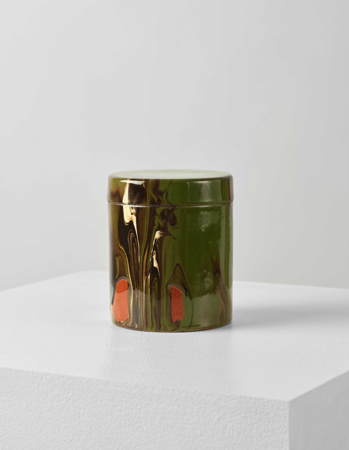 Front flat lay of a round ceramic green and terracotta marbled storage jar with lid on.
