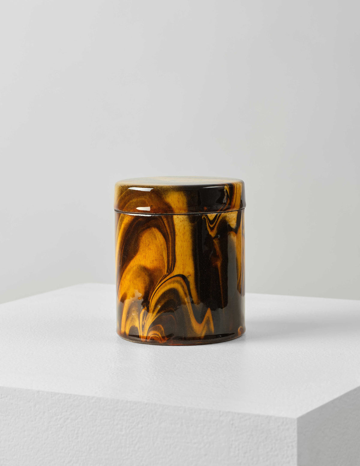 Front flat lay of a round ceramic orange and brown marbled storage jar with lid on.