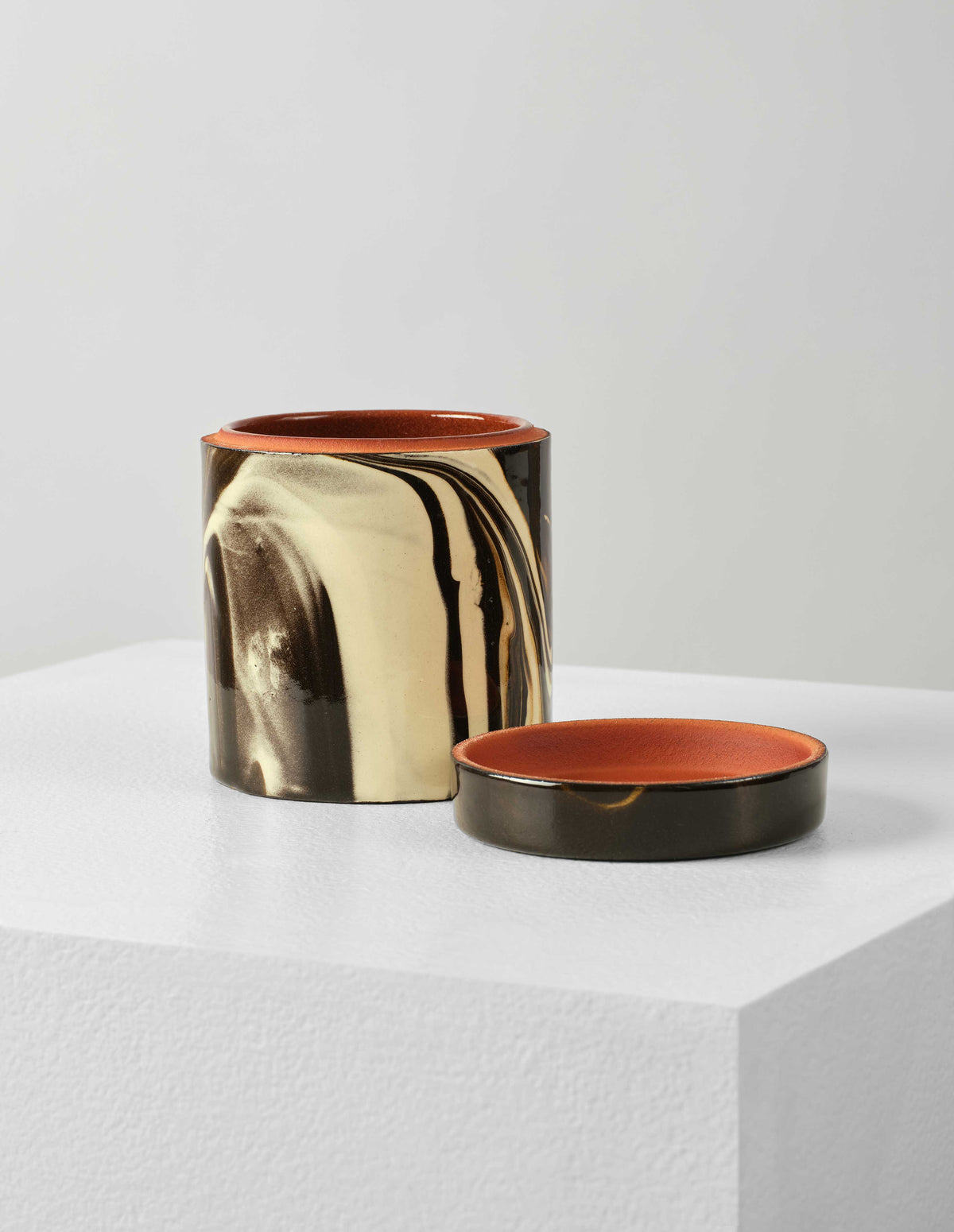 Front flat lay of a round ceramic white and brown marbled storage jar with lid off. The lid is placed next to pot, showing the terracotta coloured interior.
