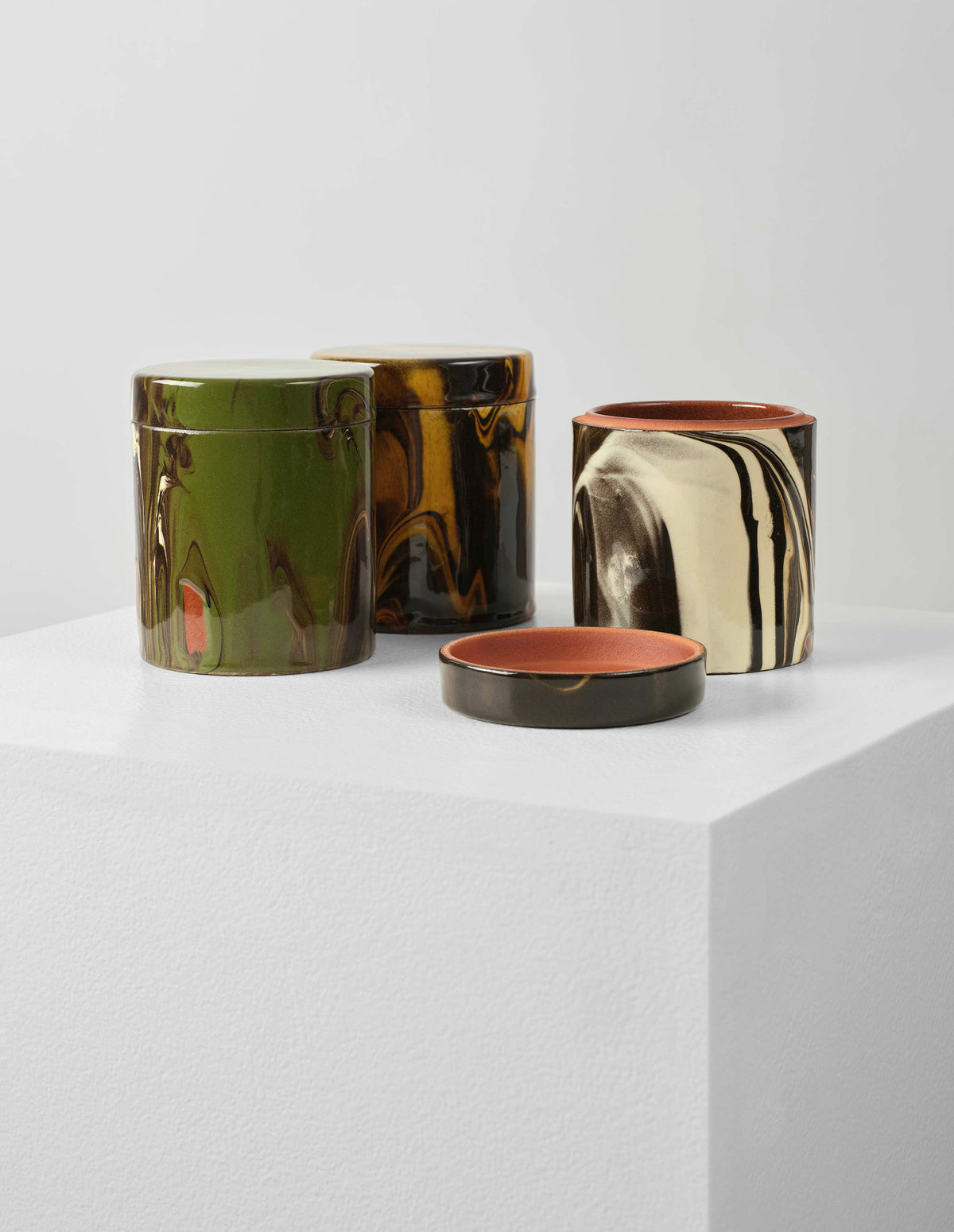 Group shot, front flat lay of three round ceramic jars, one green and terracotta, one yellow and brown and one white, brown and terracotta, with it's lid placed next to the pot to show the terracotta coloured interior of the pot.