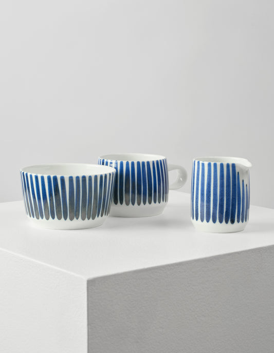 Front view of white porcelain teacup, pouring jug and bowl, all with hand painted vertical blue stripes.