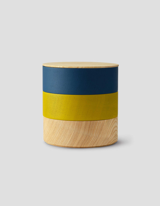 Front flat lay of a round wooden container with light natural wood lid and three stacked colour bands: dark blue, yellow and light natural wood.