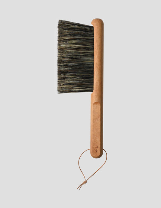 A flat lay view of the beech long handle brush with wooden handle showing the T & H logo for Turner and Harper, with natural leather hanging loop and darker hog hair bristles.