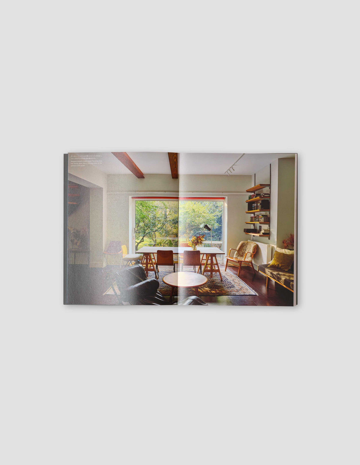 An image from the book featuring 1 photograph of a living/dining area across two pages with text in white on the left page. Flat lay image on a light grey background.