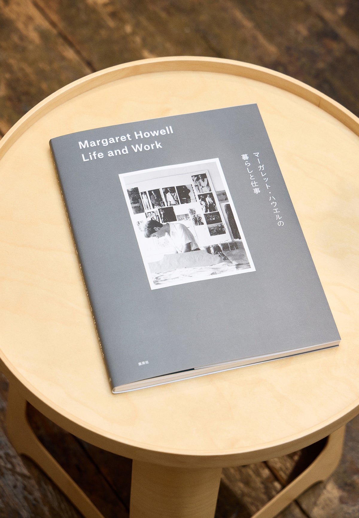 An image of 'Margaret Howell Life and Work' book placed on an Isokon plywood stool with dark brown wooden floorboards showing in the background.
