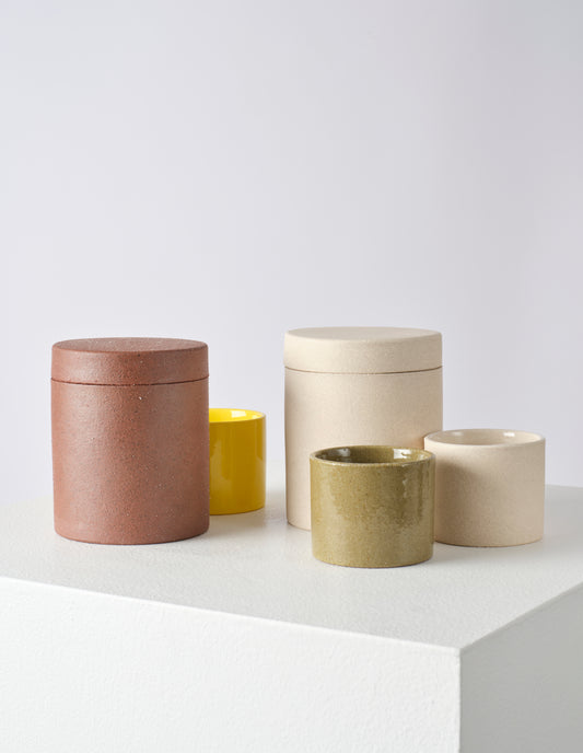 Group shot, front flat lay of five round ceramic jars and pots, two larger brown and cream pots with lids and three smaller yellow, green and cream pots with no lid.