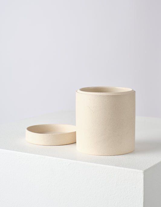 Front flat lay of a round ceramic cream storage jar with lid off. The lid is placed next to pot, showing the interior.
