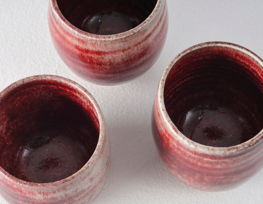 A zoomed in top down view of three oxblood beakers clearly showing the variation of the glaze on these hand thrown items.