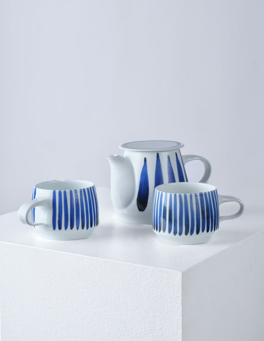 Front view of two white cups and a teapot all with hand painted vertical blue stripes.
