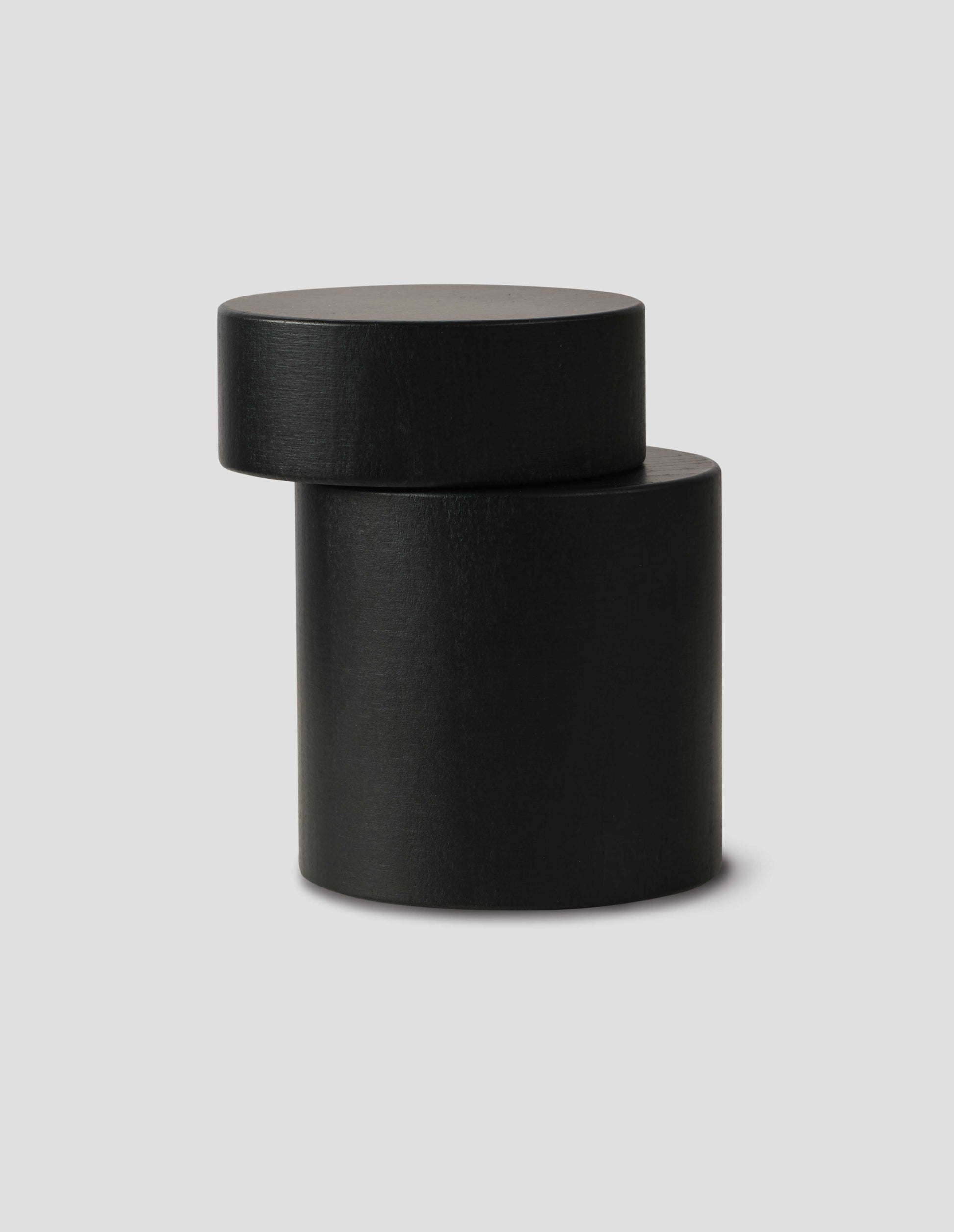A front flay lay view of a matte black cylindrical salt and pepper mill, showing the grinding functionality. 