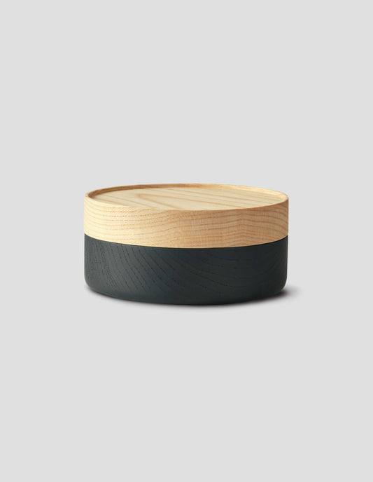 Front flat lay of a round wooden container with a light natural wood lid and matte black wooden base.