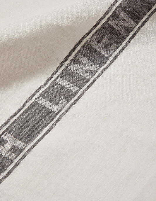 A close up view of the word linen, damask woven in white through the thick grey centre stripe of the whit linen tea towel.