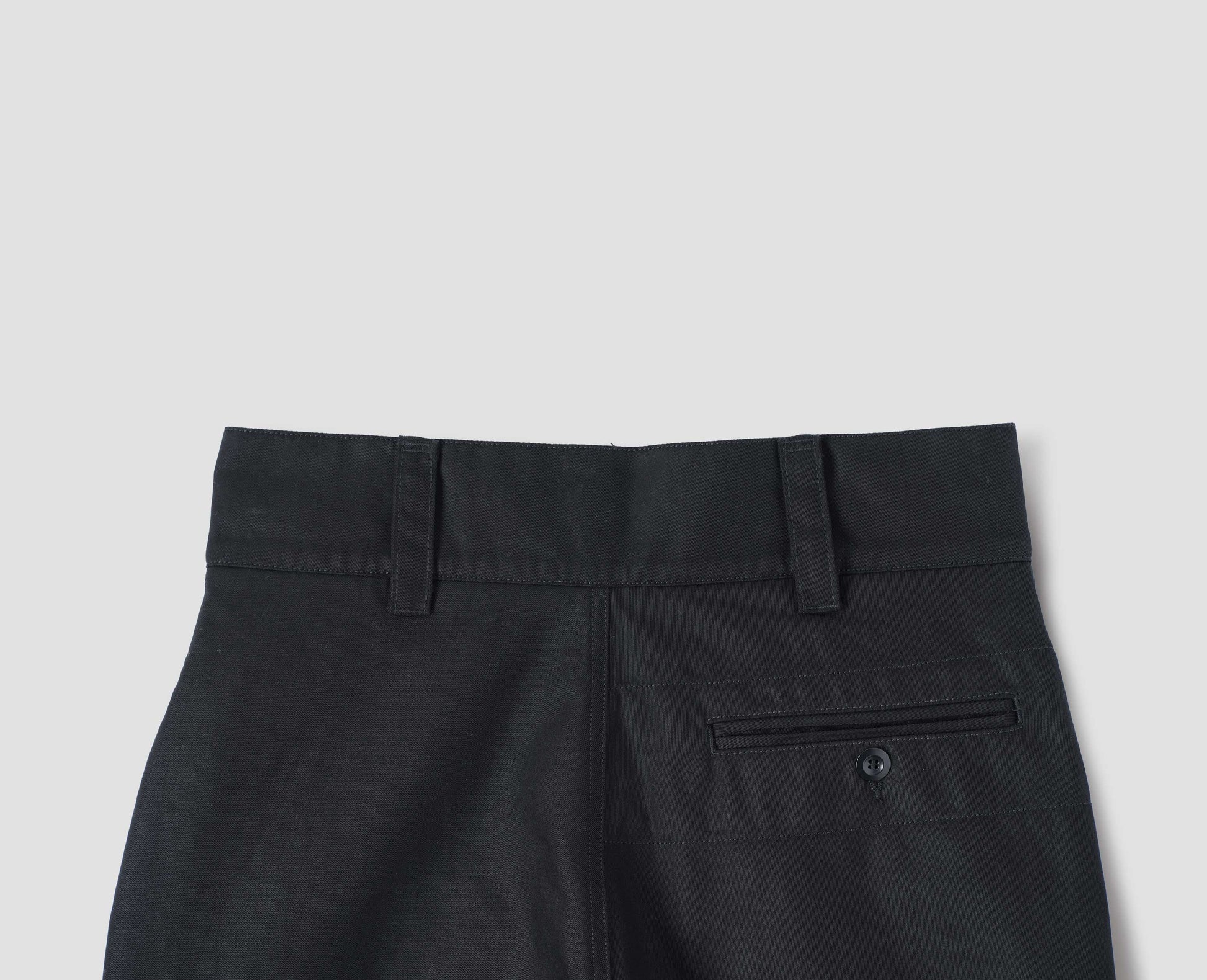 Black cotton trousers, with belt loops, button through jet pocket with stitch reinforcement detailing. Back flat lay view.