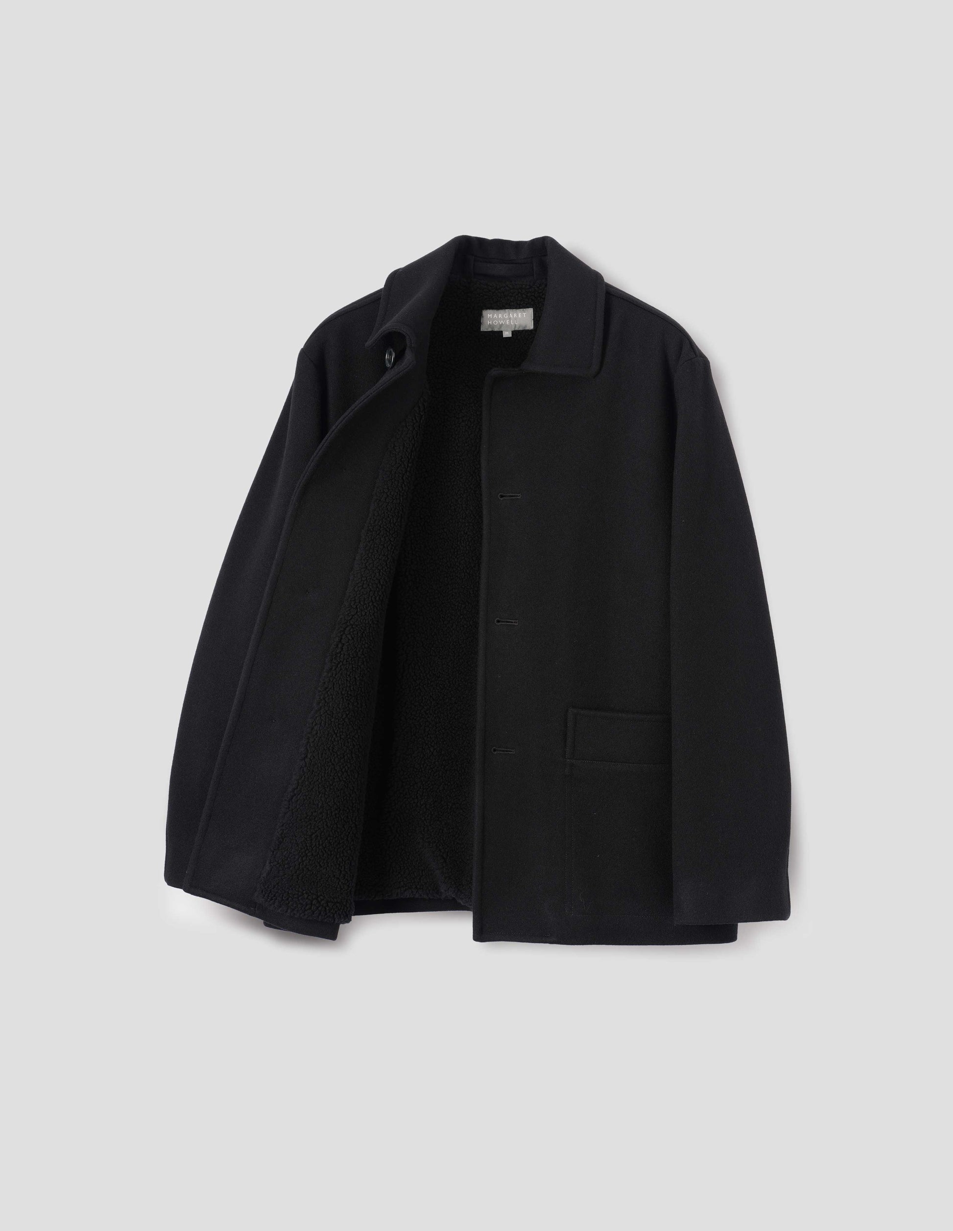 Black wool coat with contrast wool cotton fleece lining, with deep relaxed welt pockets and stitch through detailing. Finished with horn button closure. Front flat lay open view. 