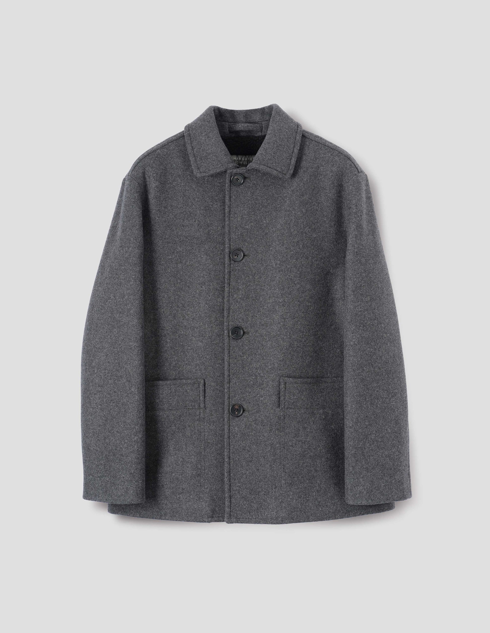 Charcoal grey wool coat with with deep relaxed welt pockets and stitch through detailing. Finished with horn button closure. Front flat lay view. 