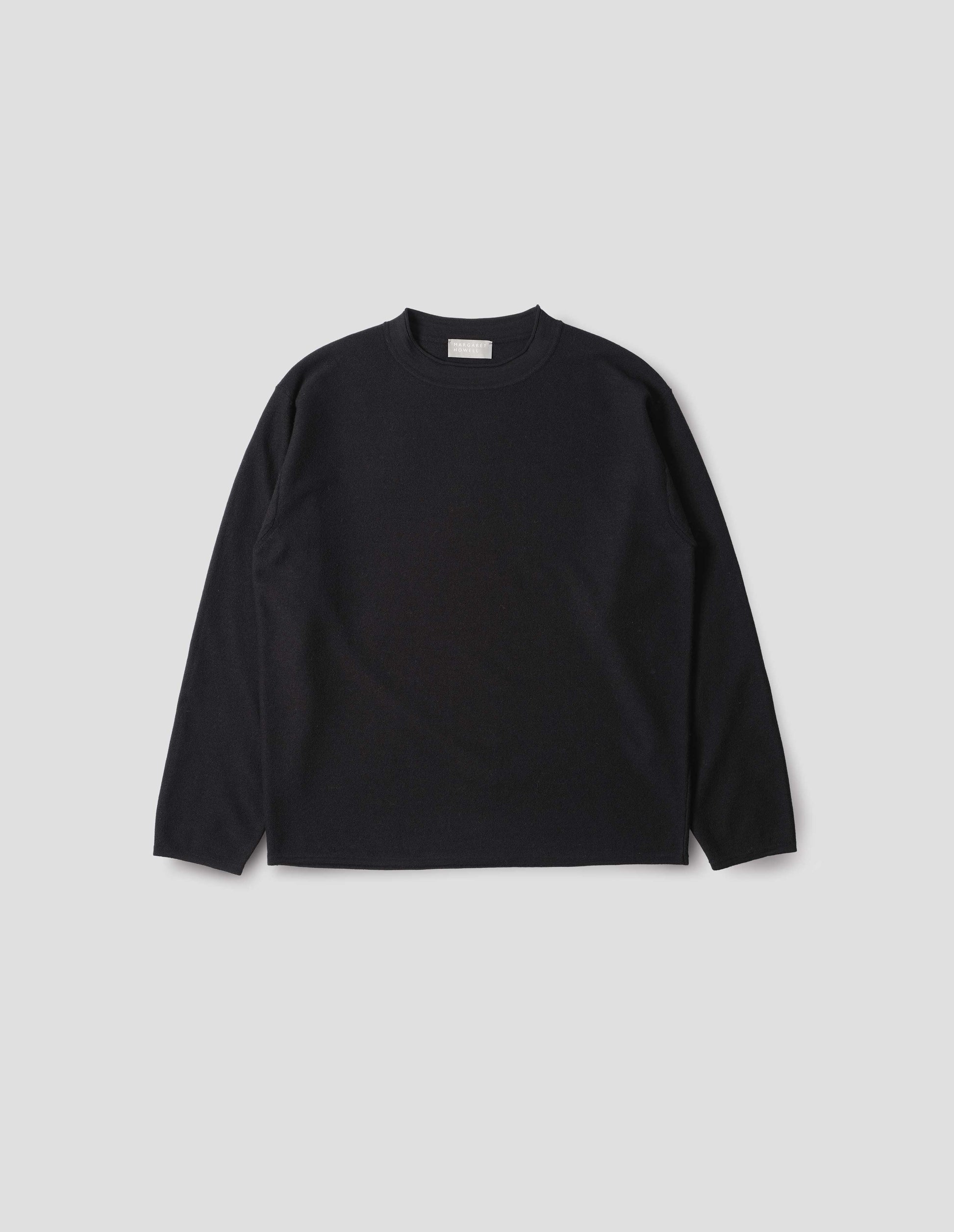 Black crew neck jumper with rolled edge detailing on neck, rib trim on cuffs and hem. Front flat lay view.
