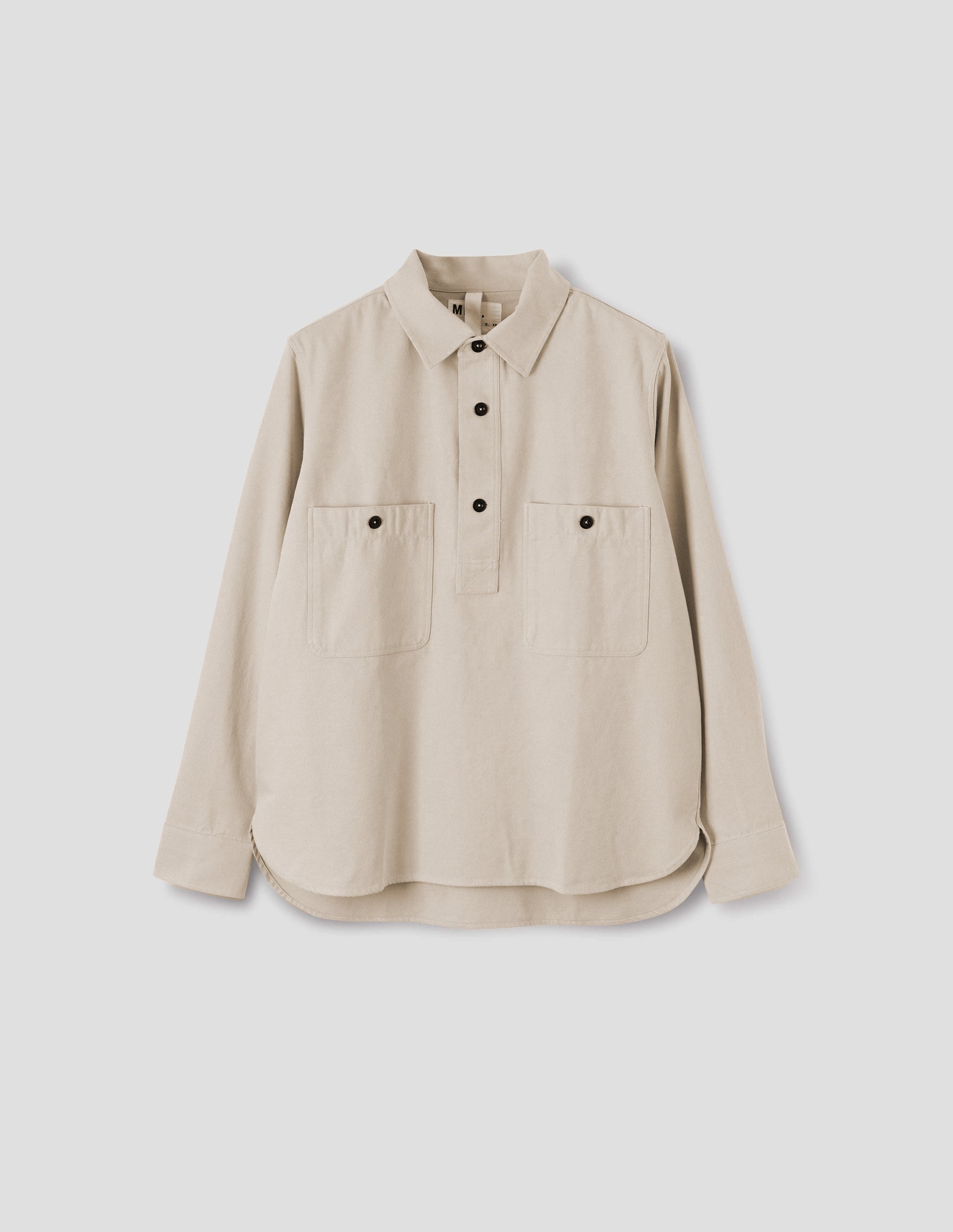 Beige overhead shirt with raised placket, box stitch detailing, button through chest patch pockets and elongated back hem. Front flat lay view.