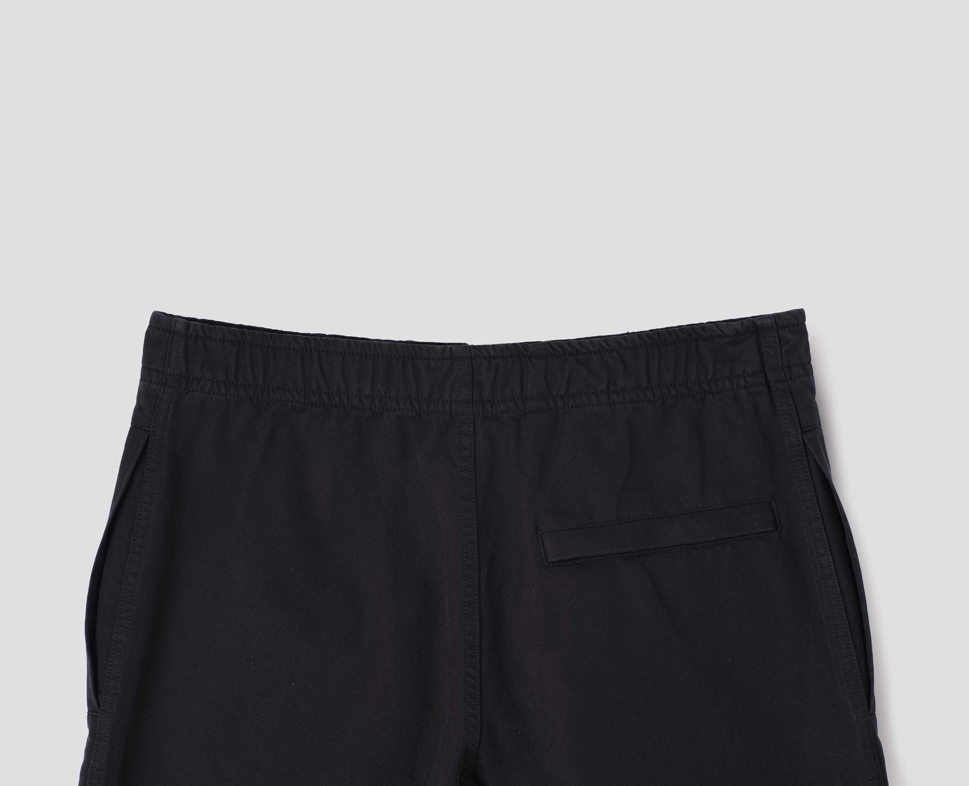 Black trousers with slant welt pockets  and press stud hem adjusters. Back flat lay view.