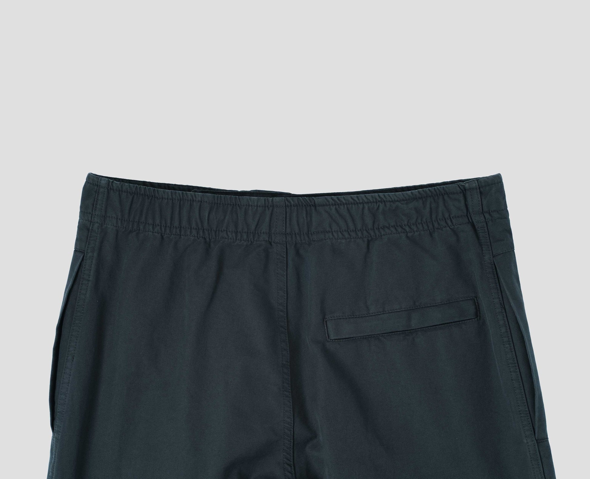 Blue trousers with slant welt pockets and press stud hem adjusters. Back flat lay view.