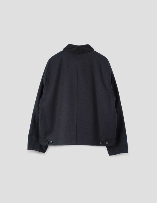 Navy blue rib neck jacket, with contrast wool rib collar, saddle sleeves, button through cuffs, raw edge detailing and button tabs to adjust the hem. Back flat lay view.