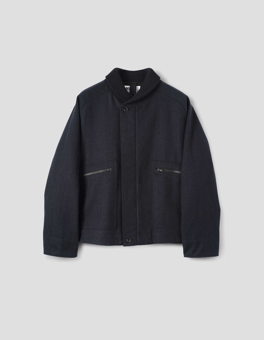 Navy blue rib neck jacket, with contrast wool rib collar, saddle sleeves, button through cuffs, patch zip pockets and raw edge detailing. Front flat lay view.