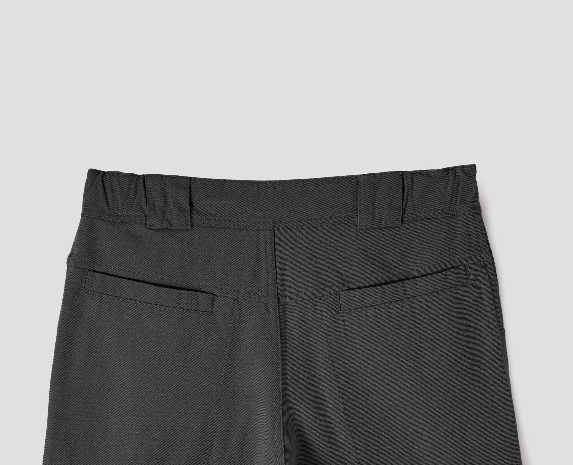 Grey trousers with side elasticated waistband, wide belt loops and stitch through welt back pockets on back yoke. Back flat lay view. 