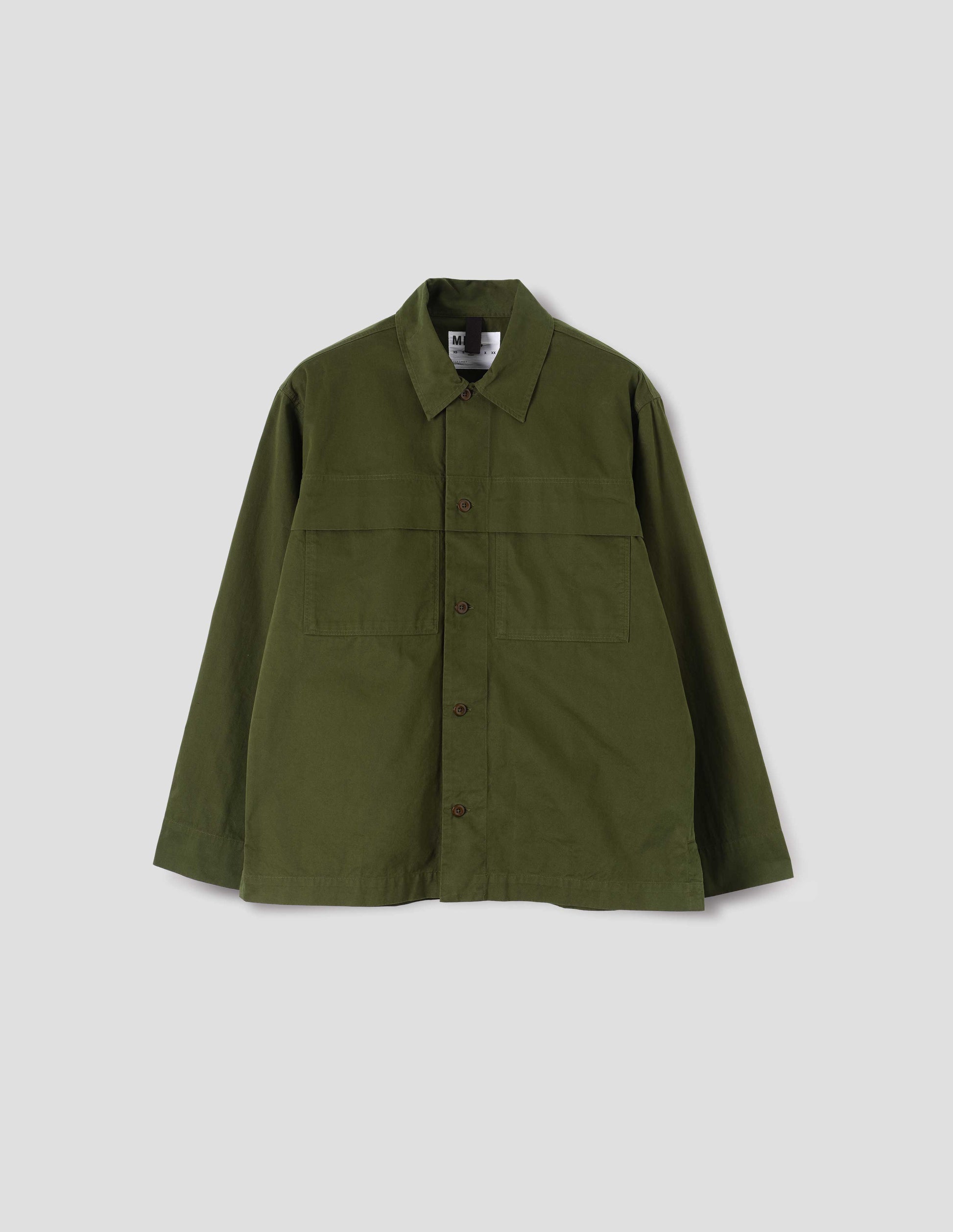 Green shirt with large storm flap patch chest pockets, corozo brace buttons, straight cuffs and vent split hem with herringbone tape detailing. Front flat lay view.