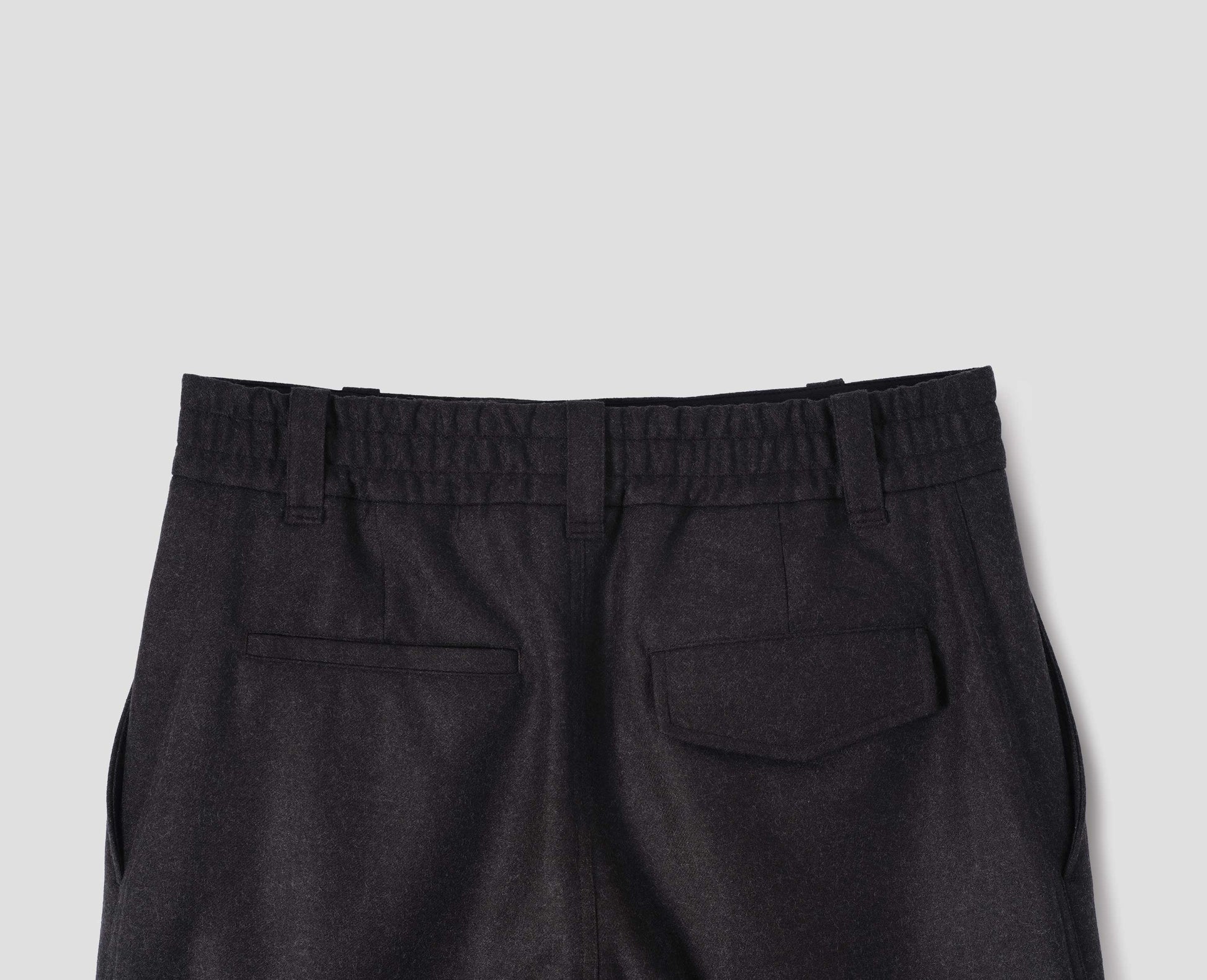 Brown wool trousers, with half elasticated waistband, belt loops and welt and concealed button fastening flap back pockets. Back flat lay view. 