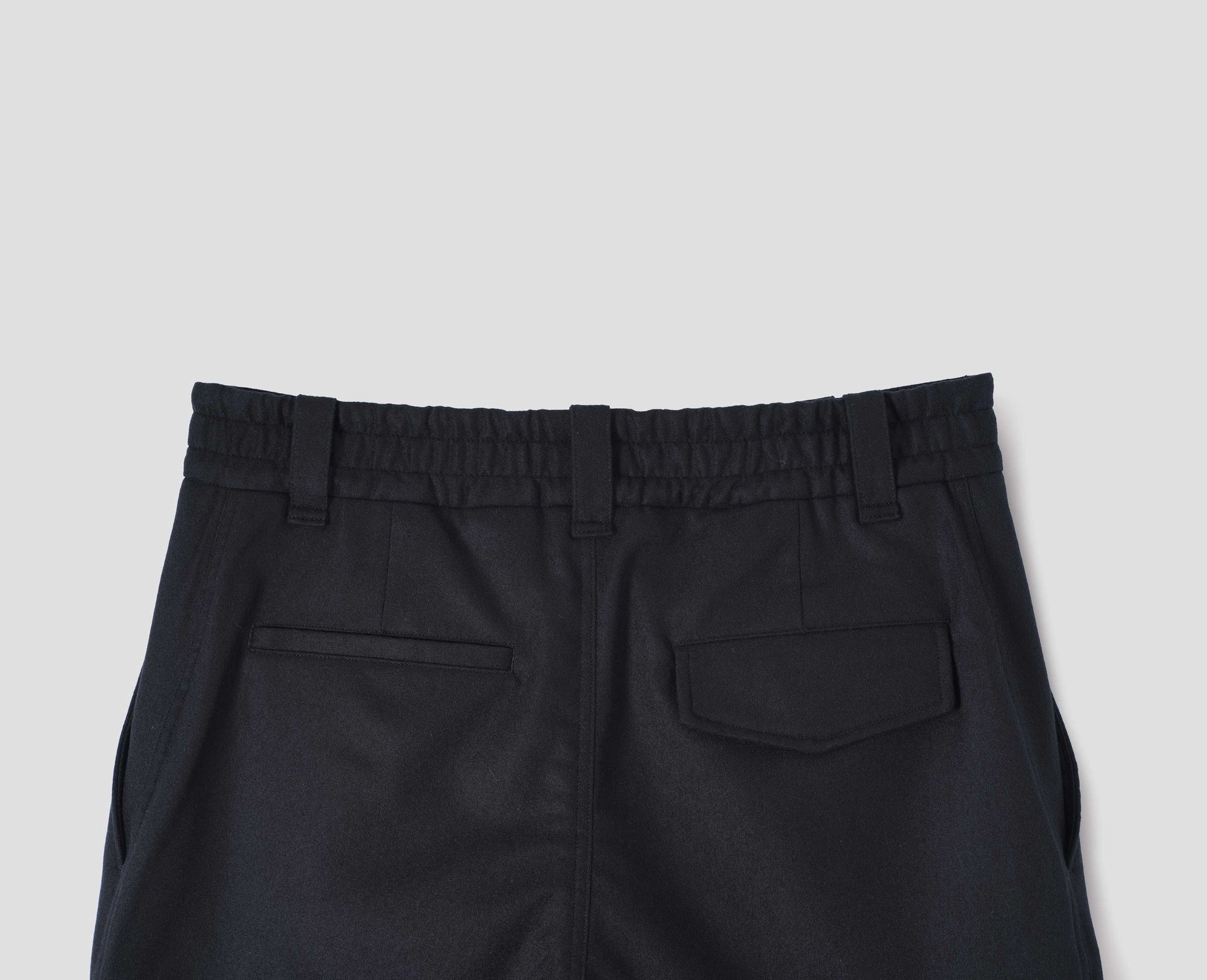 Navy blue wool trousers, with half elasticated waistband, belt loops and welt and concealed button fastening flap back pockets. Back flat lay view. 