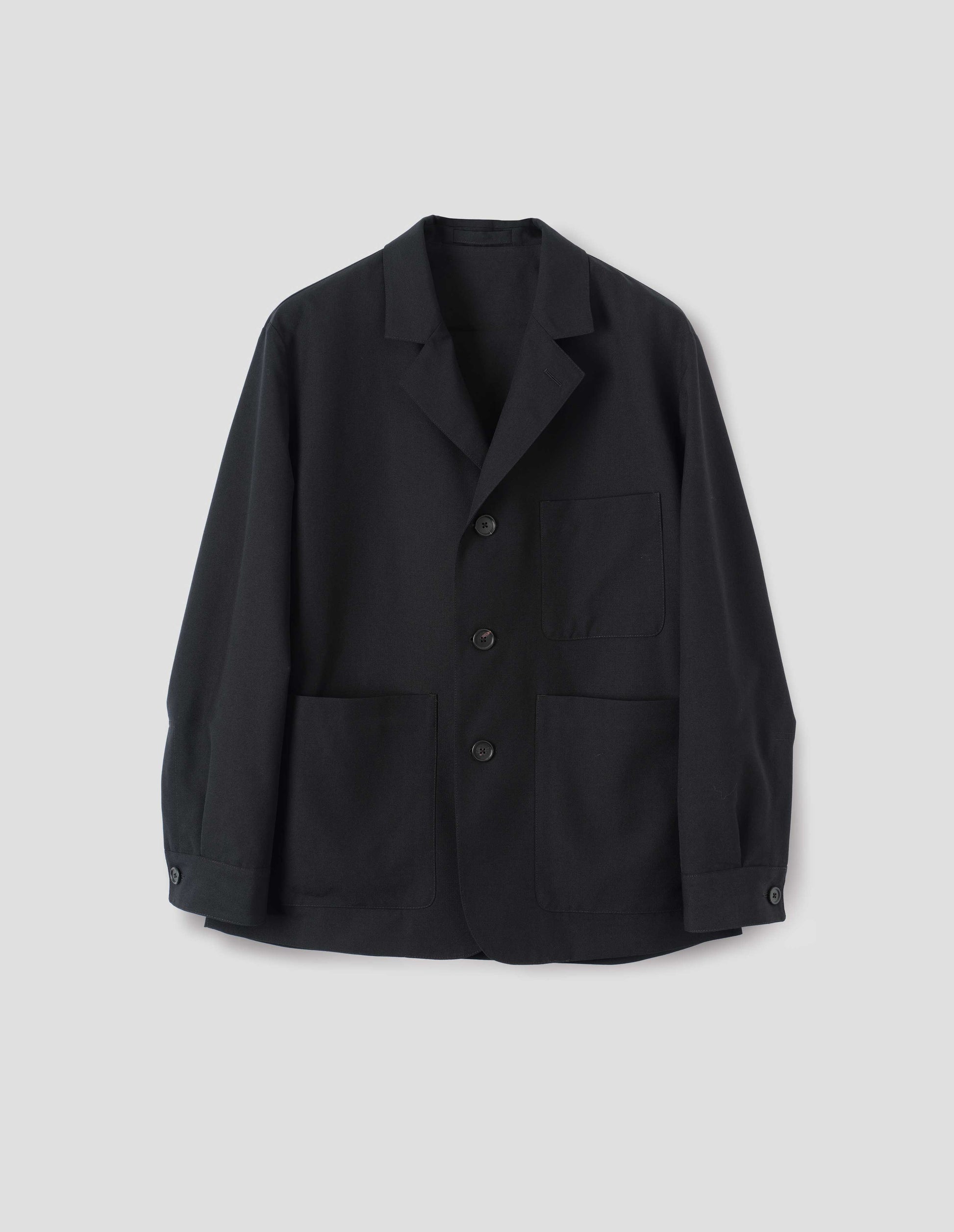 Black wool blazer with horn button fastening, deep wrap closure, shirt cuff sleeves and patch pockets. Front flat lay view.