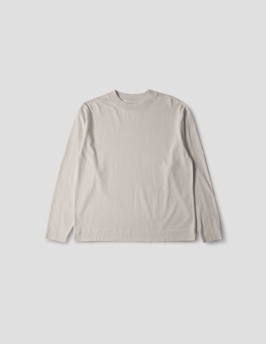 Off white cotton t shirt, with long sleeves, flatlock stitching, a deep ribbed collar and ribbed triangle insert on the shoulder, front flat lay view.