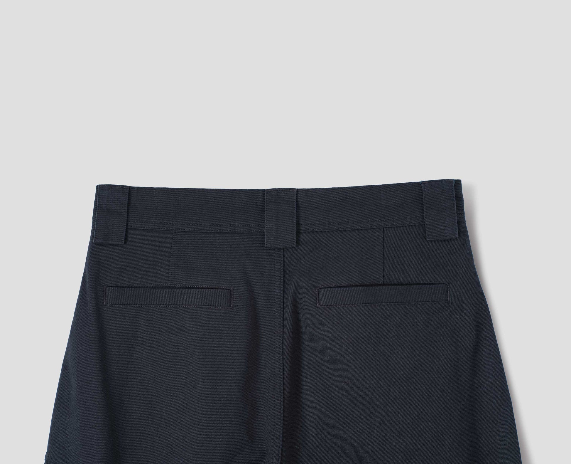 Dark blue cotton trousers, with wide belt loops and two  welt pockets, back flat lay view.