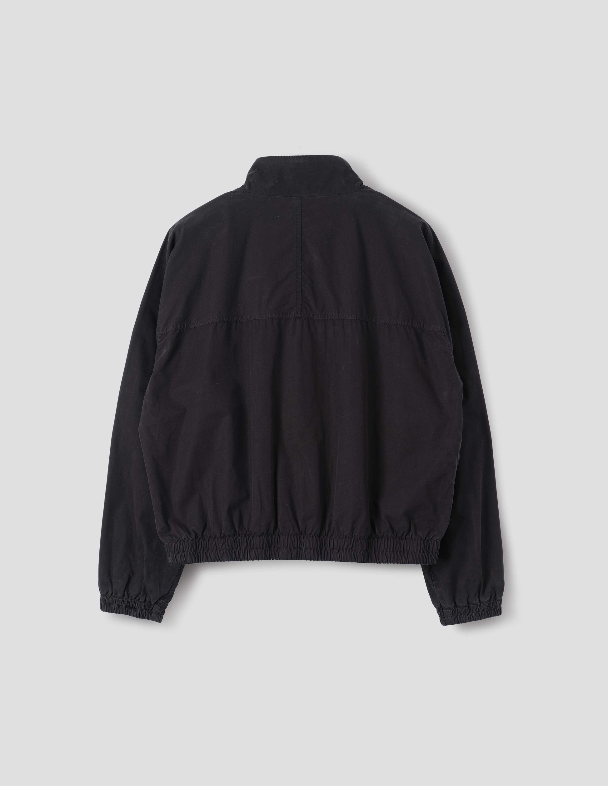 Black cotton poplin track jacket with stand collar, raglan sleeves, elasticated hem and cuffs. Back flat lay view.