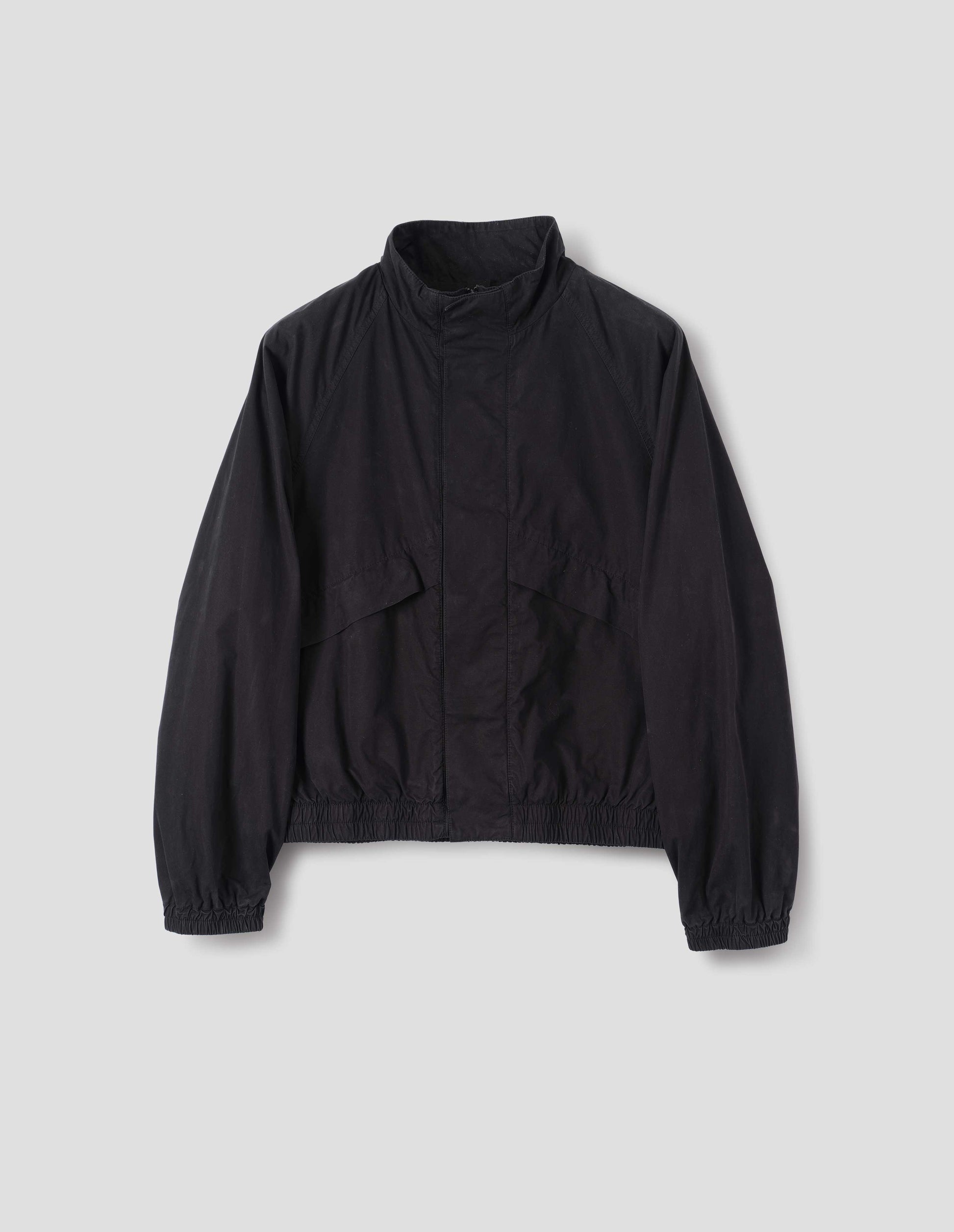 Black cotton poplin track jacket with stand collar, raglan sleeves, concealed zip closure  and press stud fastening and elasticated hem and cuffs. Large slanted front pockets. Front flat lay view. 