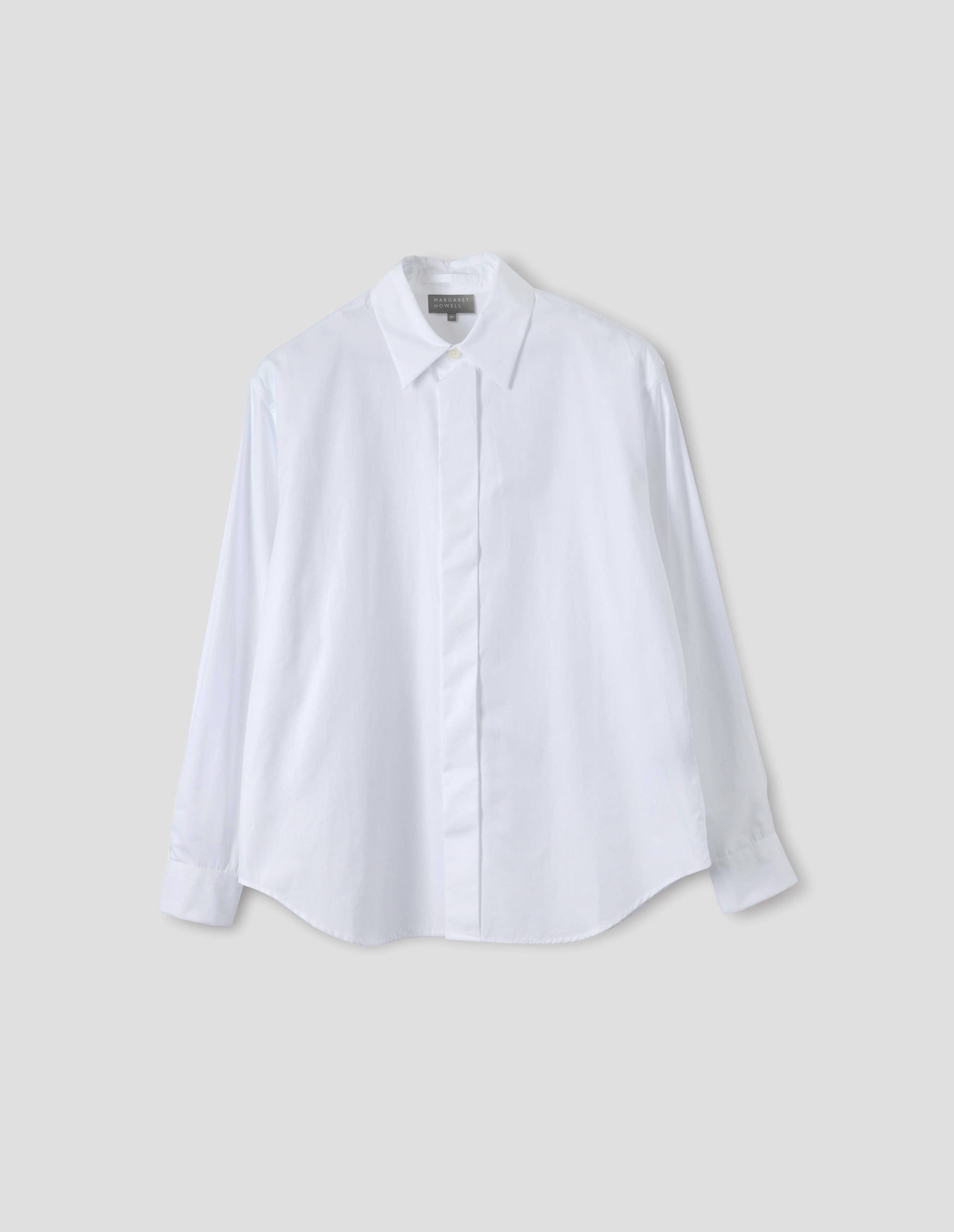 White cotton shirt with concealed button placket and mother of pearl button on collar, hanger loop on back neck and curved hem. Front flat lay view.