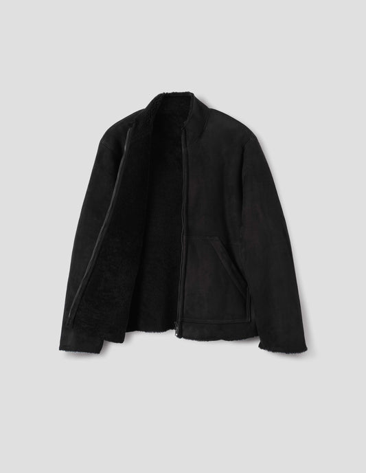Black sheepskin jacket with zip-through front, partial funnel neck with raw edge, slanted front half kangaroo pockets, raw edges on sleeves and hem, and curly merino inside. Open flat lay view.