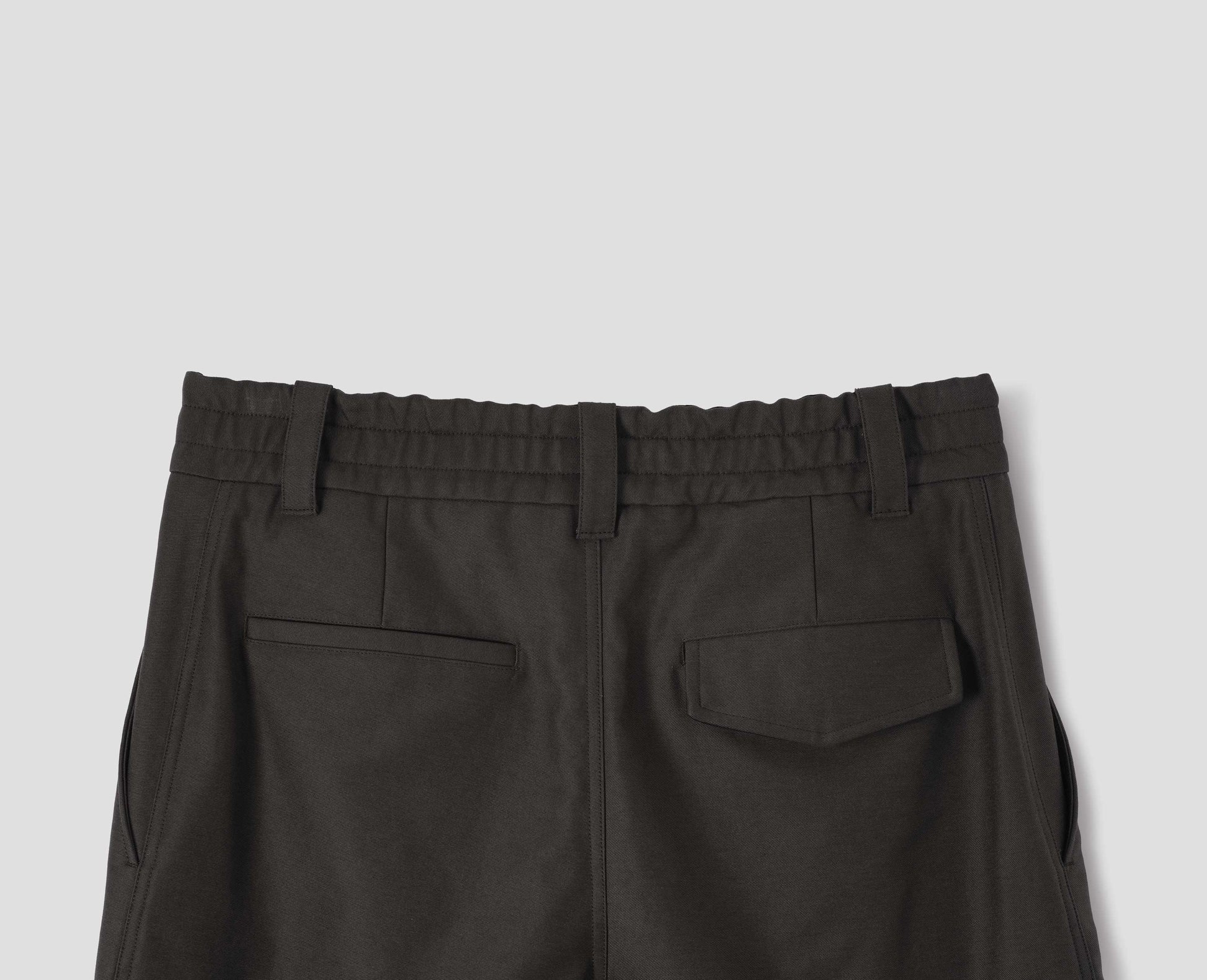 Grey cotton trousers with half-elasticated waistband with belt loops, slant side pockets, and welt and flap back pocket with concealed horn button fastening. Back flat lay view.