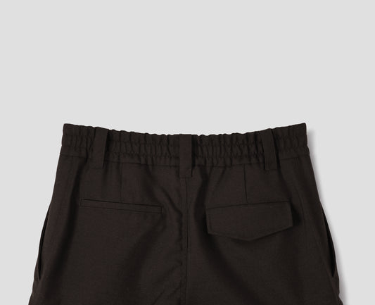 Dark brown wool trousers with half-elasticated waist with belt loops, slant side pockets, and one welt back pocket and one flap back pocket with concealed button fastening. Back flat lay view.