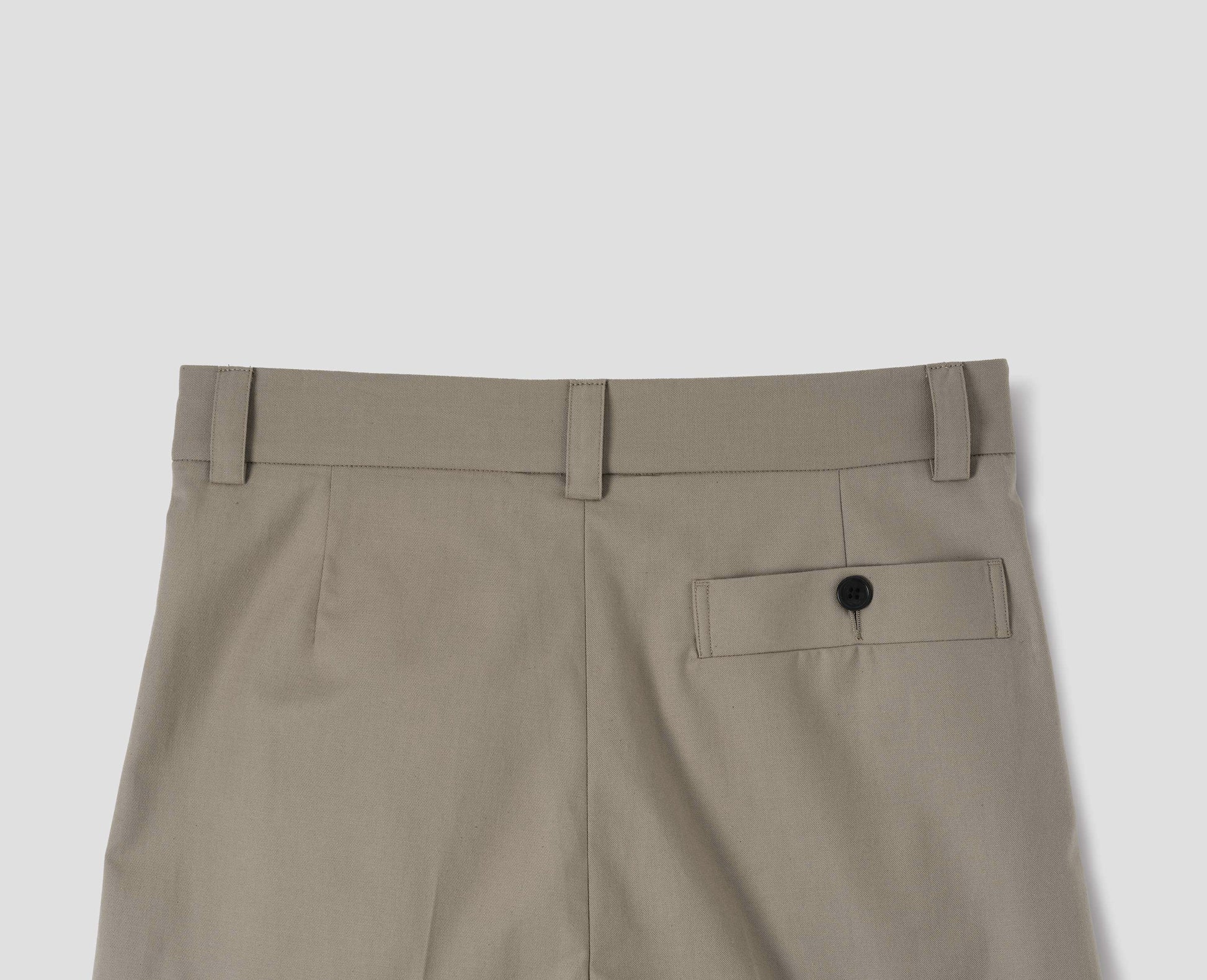 Beige cotton trousers with belt loops and deep horn button-through welt back pocket. Back flat lay view.