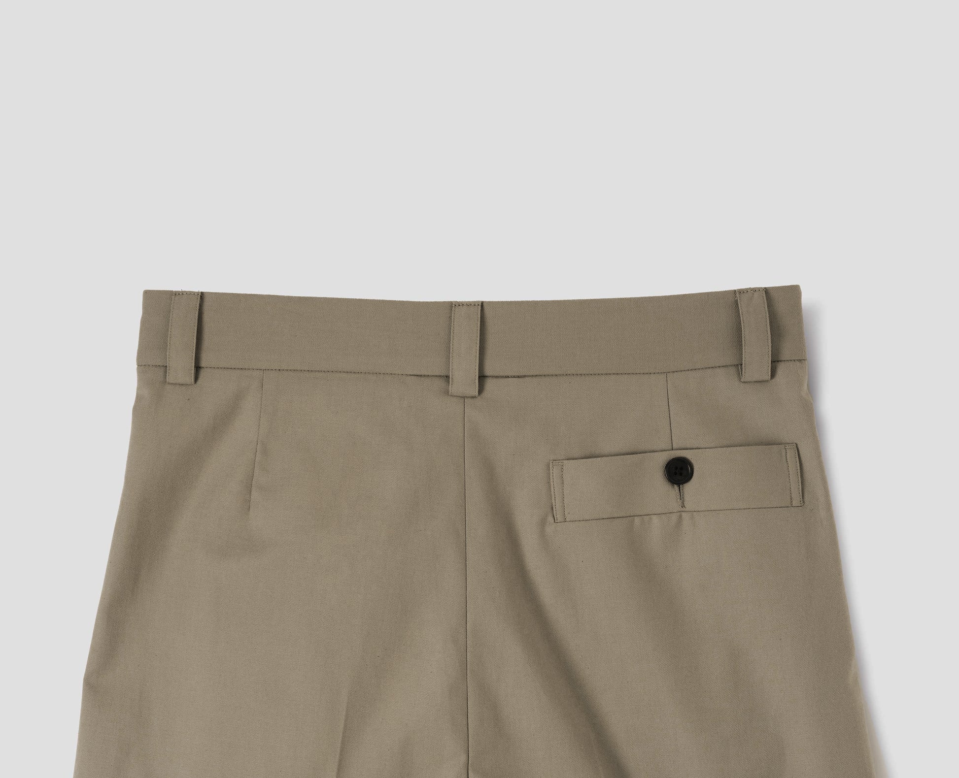 Beige cotton trousers with belt loops and deep horn button-through welt back pocket. Back flat lay view.